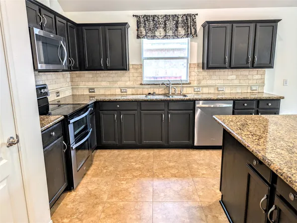 a large kitchen with stainless steel appliances kitchen island granite countertop a stove and a sink