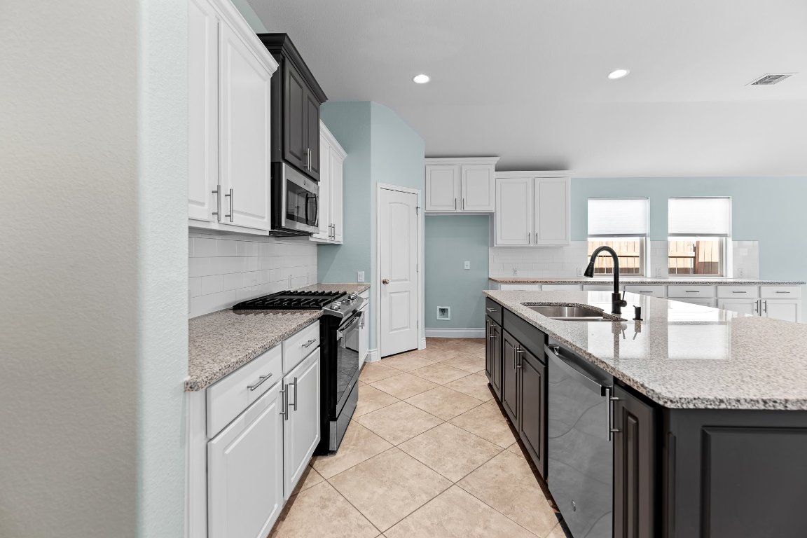 217 Serrano Street Georgetown, TX 78628 - Photo 10 of 27 a large kitchen with granite countertop a sink and dishwasher a stove top oven with wooden floor