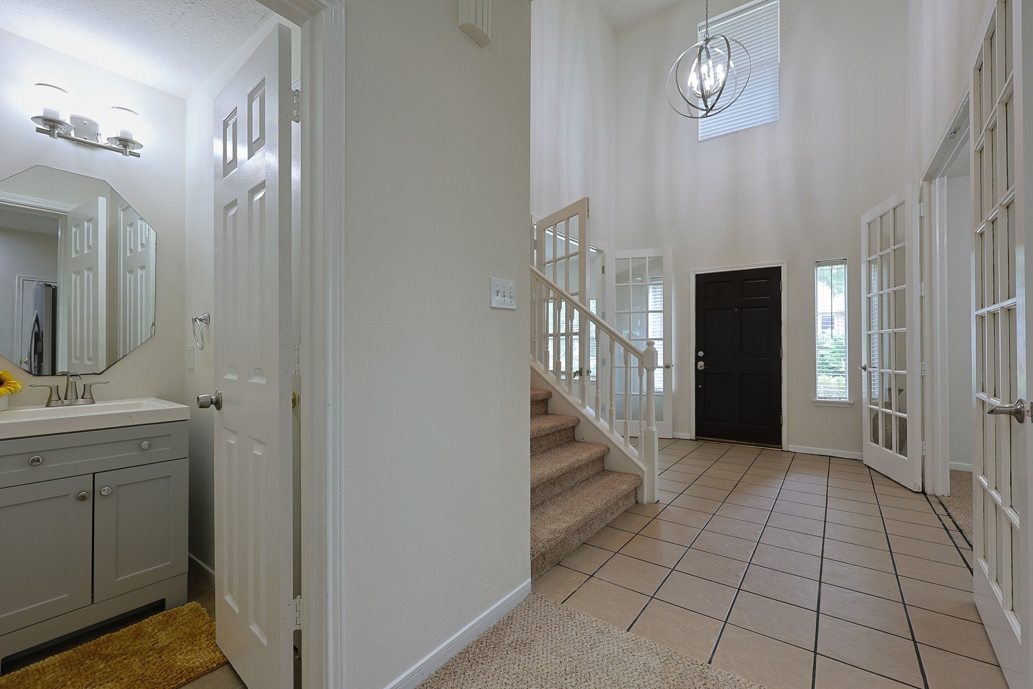 23019 Eastgate Village Drive Spring, TX 77373 - Photo 16 of 46 Bright entryway with a modern light fixture and tiled flooring. It features a staircase with carpeted steps, a dark front door, and glass-paned double doors leading to adjacent rooms.