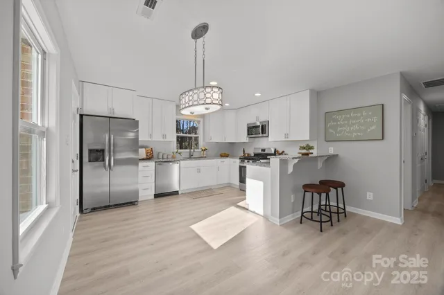 a kitchen with stainless steel appliances kitchen island granite countertop a refrigerator a stove and white cabinets with wooden floor