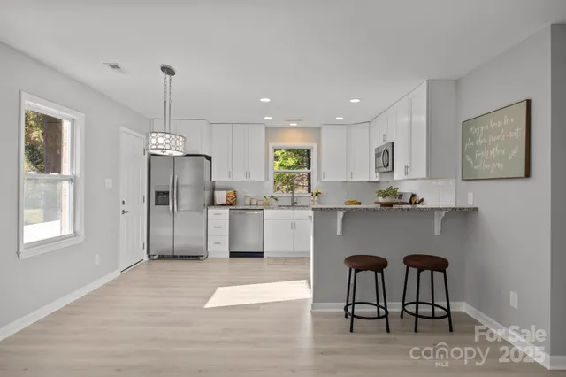 a kitchen with stainless steel appliances granite countertop a refrigerator a stove a sink dishwasher a dining table and chairs with wooden floor
