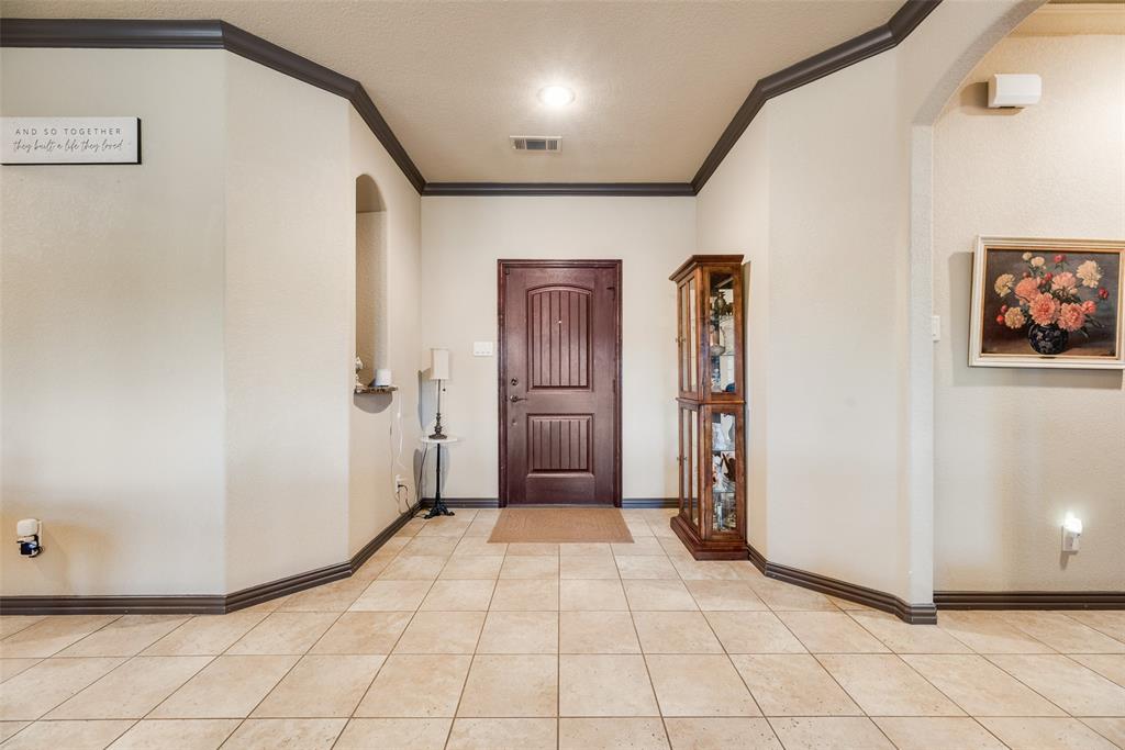 1132 Chartres Street Kaufman, TX 75142 - Photo 3 of 25 Entryway featuring light-toned tile flooring, a dark wood-finish entry door with paneling, and contrasting dark-stained crown molding and baseboards