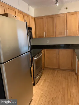 a view of a refrigerator in kitchen and an empty room with wooden floor