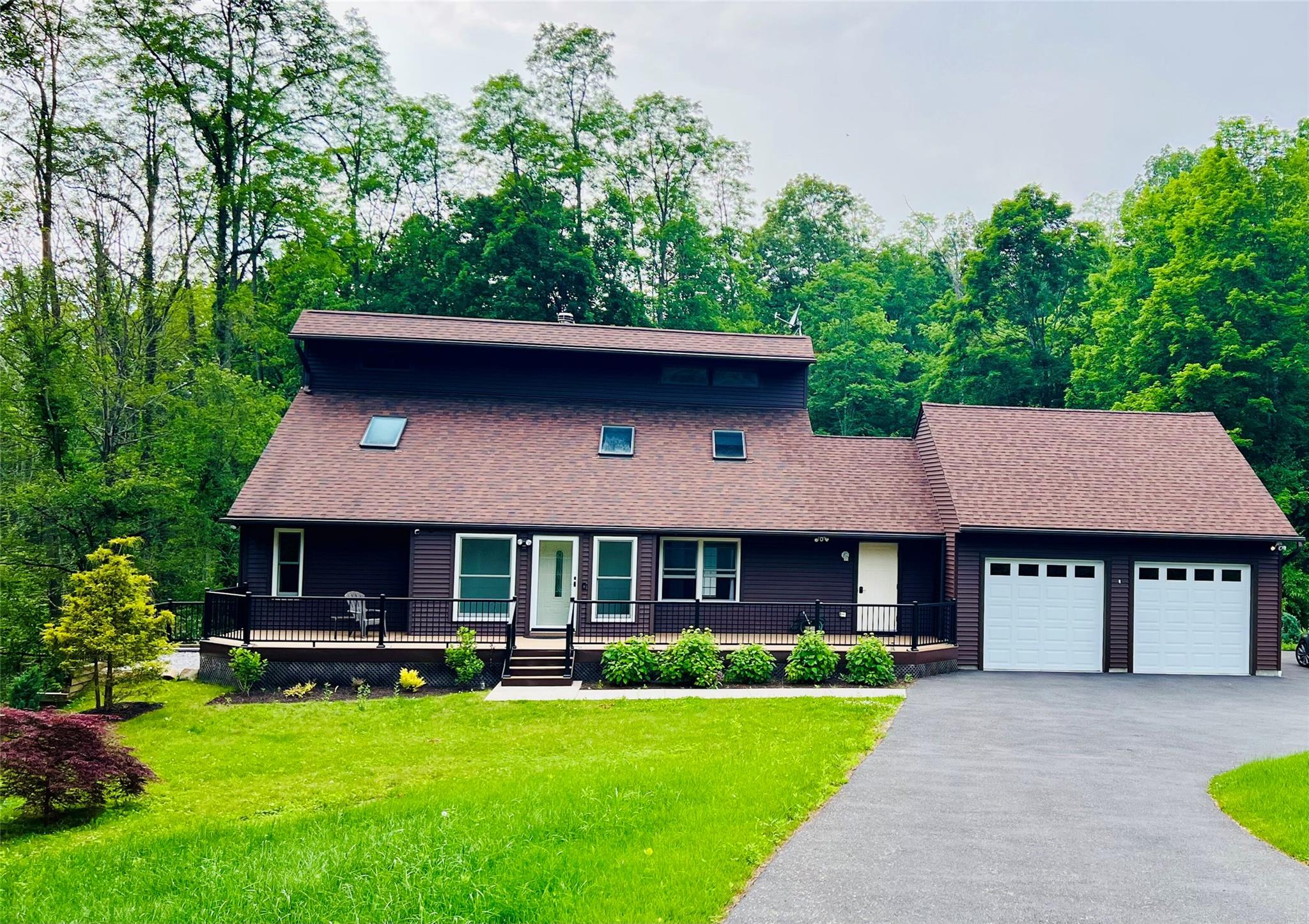 View of front of house with an attached garage, a porch, a front lawn, and a shingled roof