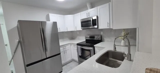 a kitchen with stainless steel appliances a refrigerator a sink and white cabinets