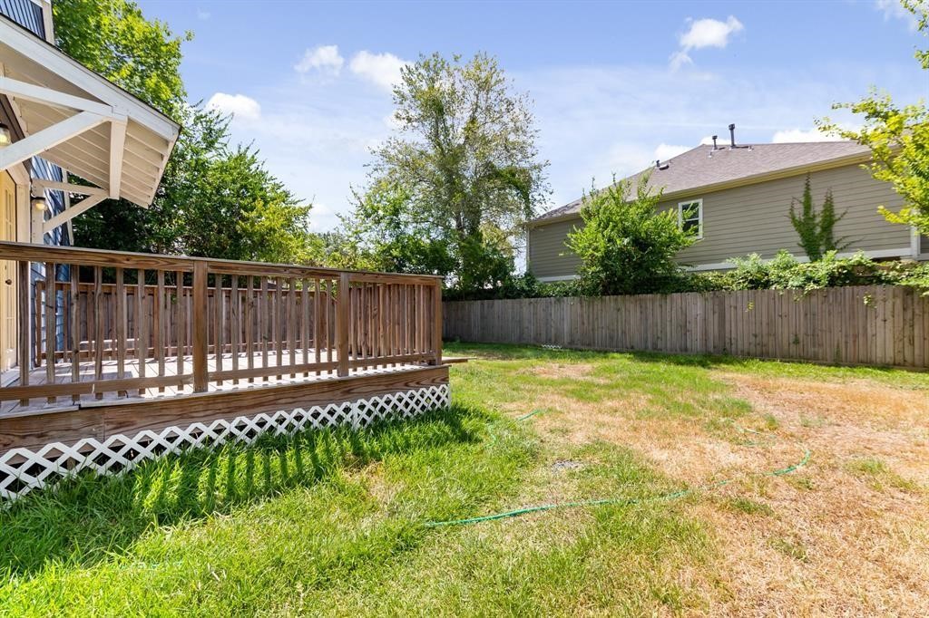 1305 Idylwild Street Houston, TX 77009 - Photo 30 of 31 This photo showcases a spacious backyard with a wooden deck attached to the house. The yard is fenced for privacy and has a mix of grass and shaded areas, ideal for outdoor activities or gardening.