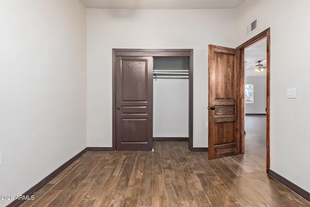 a view of empty room with wooden floor and kitchen