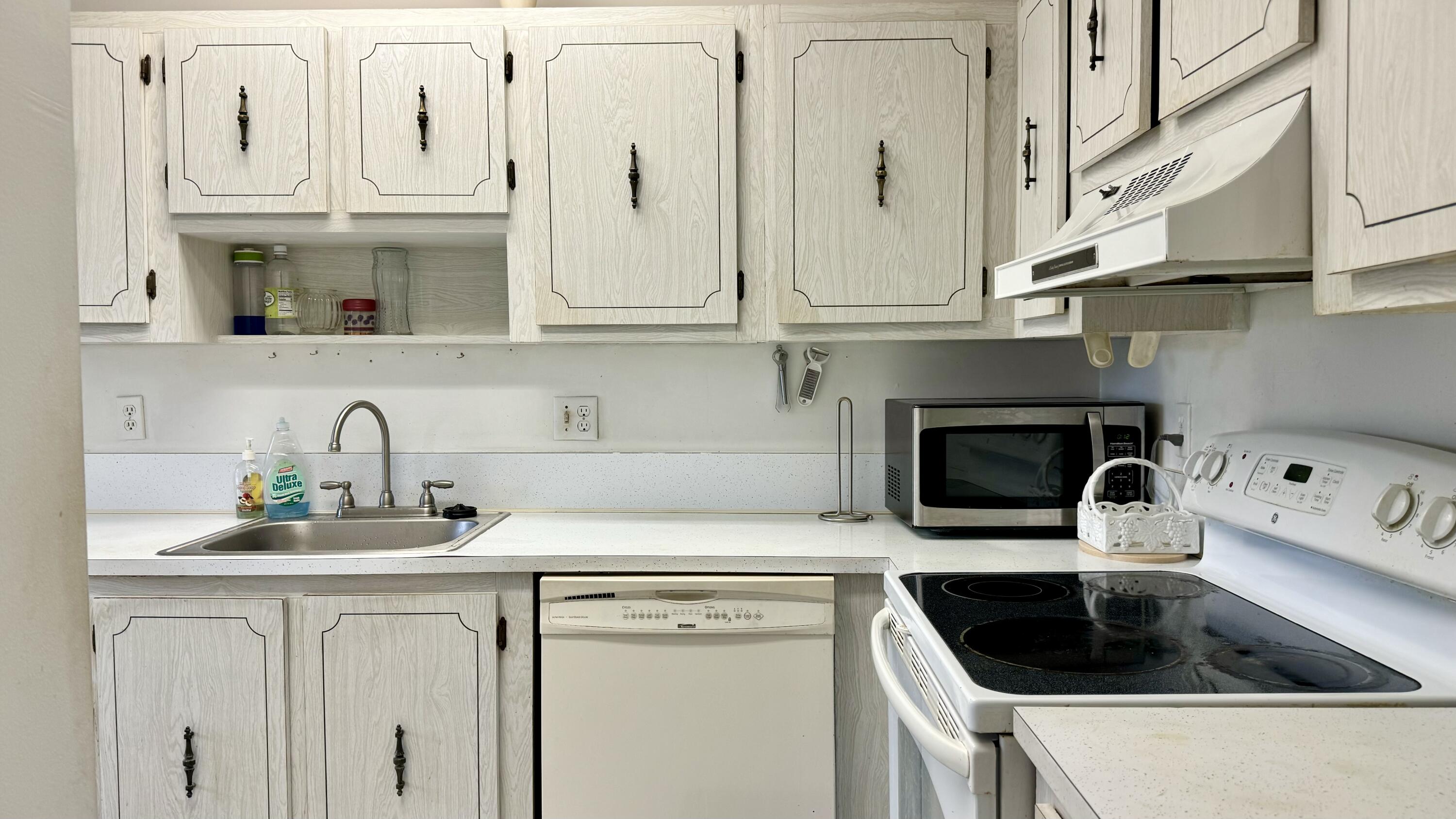 1551 Northwest 20th Avenue, Unit 102 Delray Beach, FL 33445 - Photo 4 of 18 a kitchen with white cabinets and a stove with wooden floor