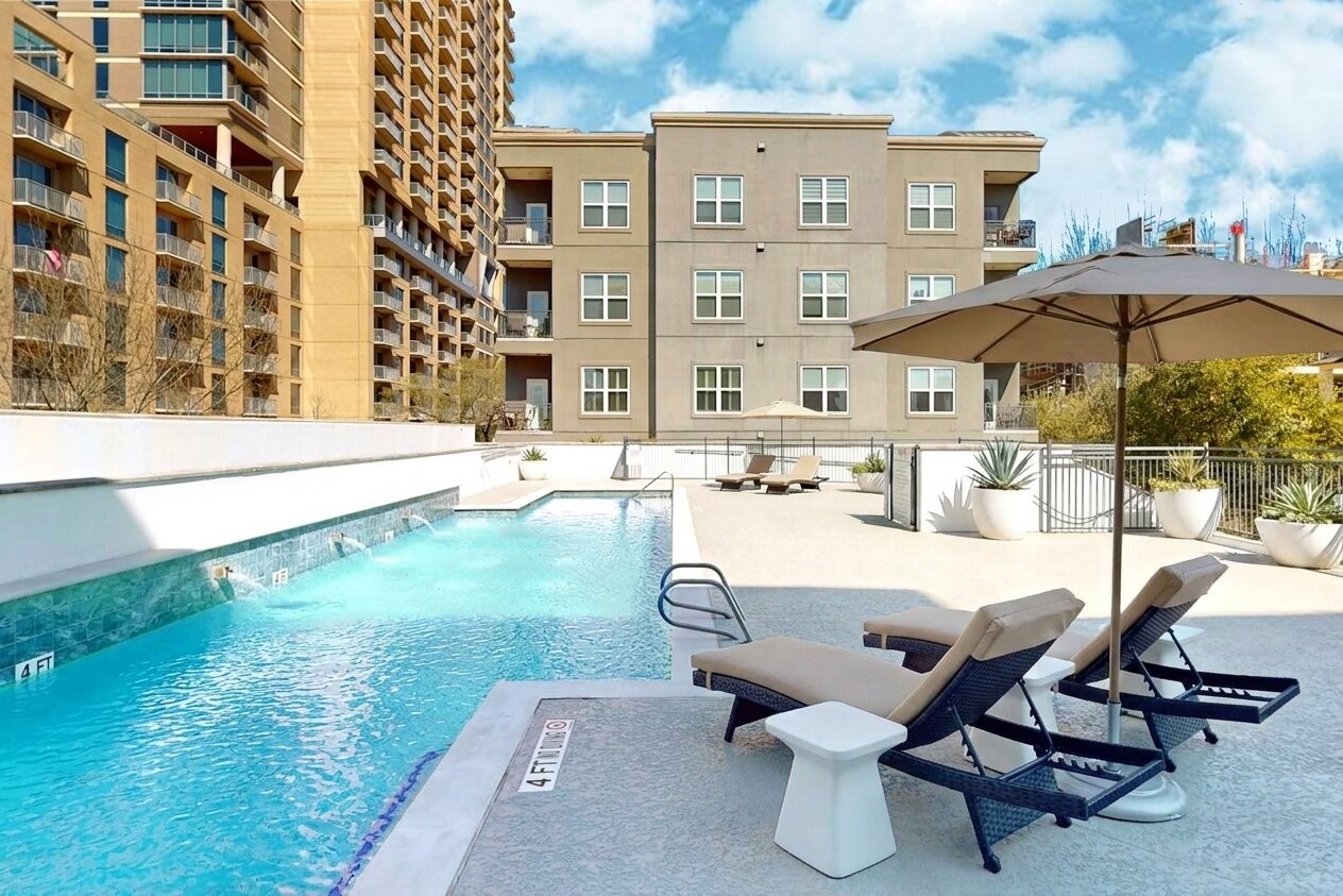 1010 Rosine Street, Unit 29 Houston, TX 77019 - Photo 6 of 16 This photo showcases a modern apartment complex with a spacious outdoor pool area. It features comfortable lounge chairs, umbrellas for shade, and is surrounded by well-maintained landscaping and adjacent buildings, offering a relaxing and stylish environment. (Virtual Staging)