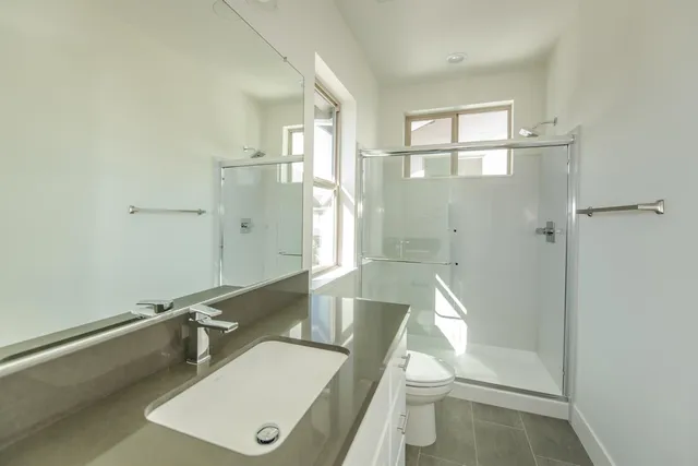 a bathroom with a granite countertop sink a toilet a mirror and shower
