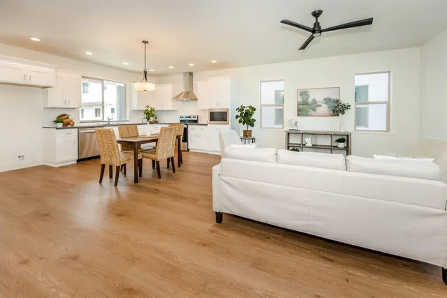 a living room with couches kitchen view and a dining table with wooden floor
