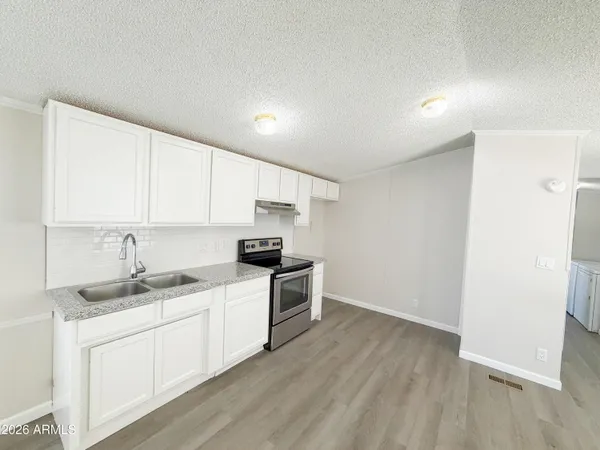 a kitchen with granite countertop a stove a sink and white cabinets with wooden floor
