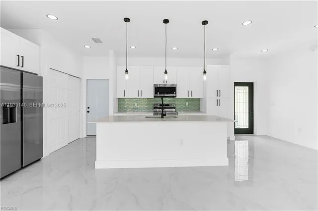 a large white kitchen with stainless steel appliances granite countertop a stove a sink a refrigerator and a chandelier