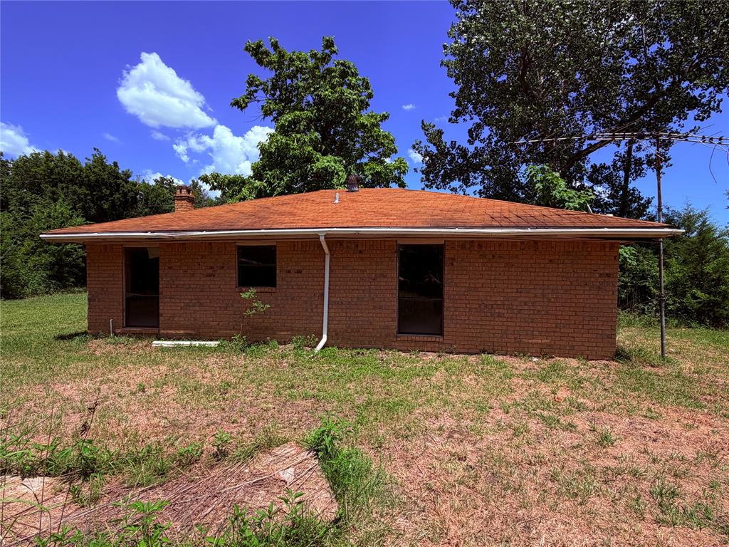 690 County Road Brookston, TX 75421 - Photo 5 of 10 Brick exterior featuring a red shingle roof, white gutters, and a visible chimney