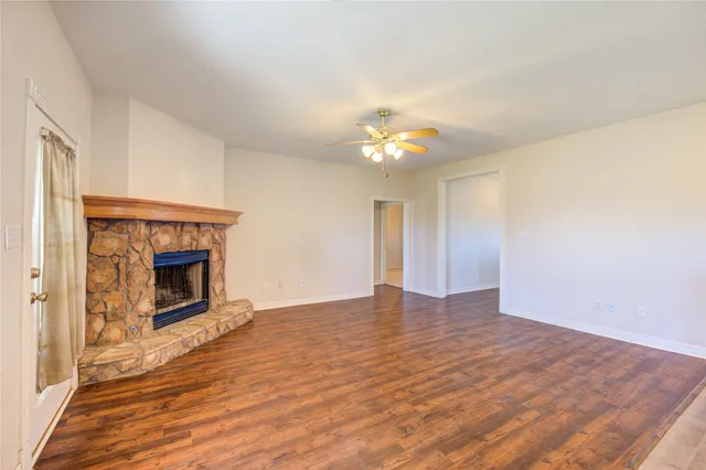a view of an empty room with wooden floor fireplace and a window
