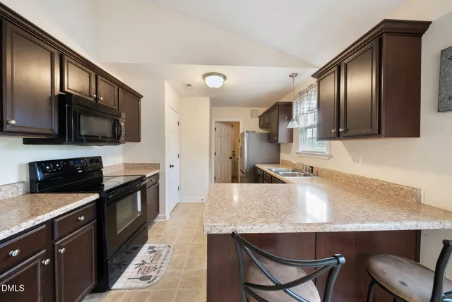 a kitchen with stainless steel appliances granite countertop a sink a stove a refrigerator cabinets and chairs