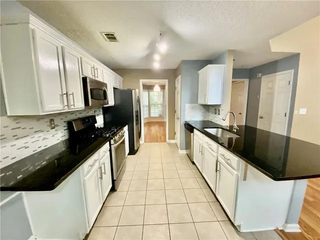 a large white kitchen with stainless steel appliances kitchen island granite countertop a large counter top and a stove top oven