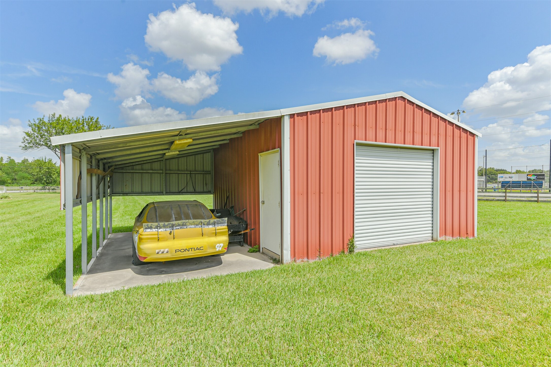 307 West Hufsmith Road Tomball, TX 77375 - Photo 43 of 44 Spacious red metal garage with attached carport, perfect for vehicle storage or a workshop, set on a lush green lawn.
