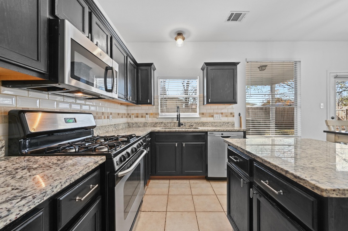 1451 Roxanne's Run Pflugerville, TX 78660 - Photo 7 of 17 a kitchen with stainless steel appliances granite countertop a stove sink and cabinets