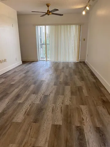 an empty room with wooden floor fan and windows