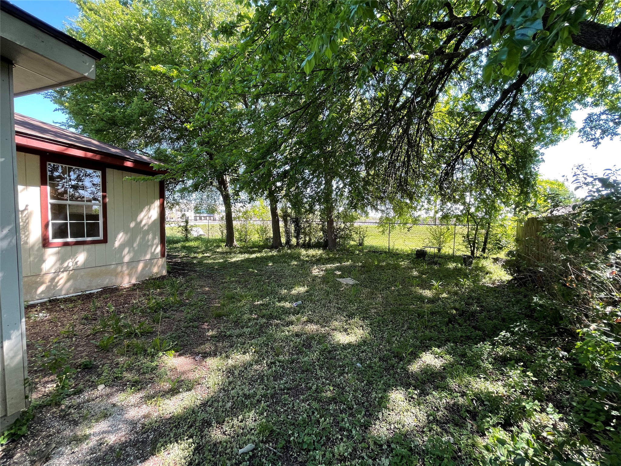 2004 Maple Street Georgetown, TX 78626 - Photo 27 of 31 Rear exterior of the property featuring a light-colored siding, a window with red trim, and a dark shingle roof