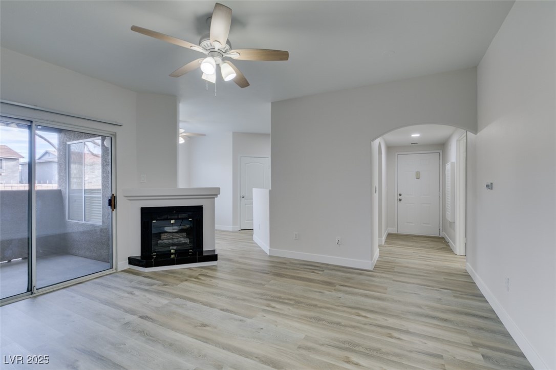 5525 West Flamingo Road, Unit 1028 Las Vegas, NV 89103 - Photo 11 of 42 Unfurnished living room with light wood-style floors, a glass covered fireplace, arched walkways, and a ceiling fan