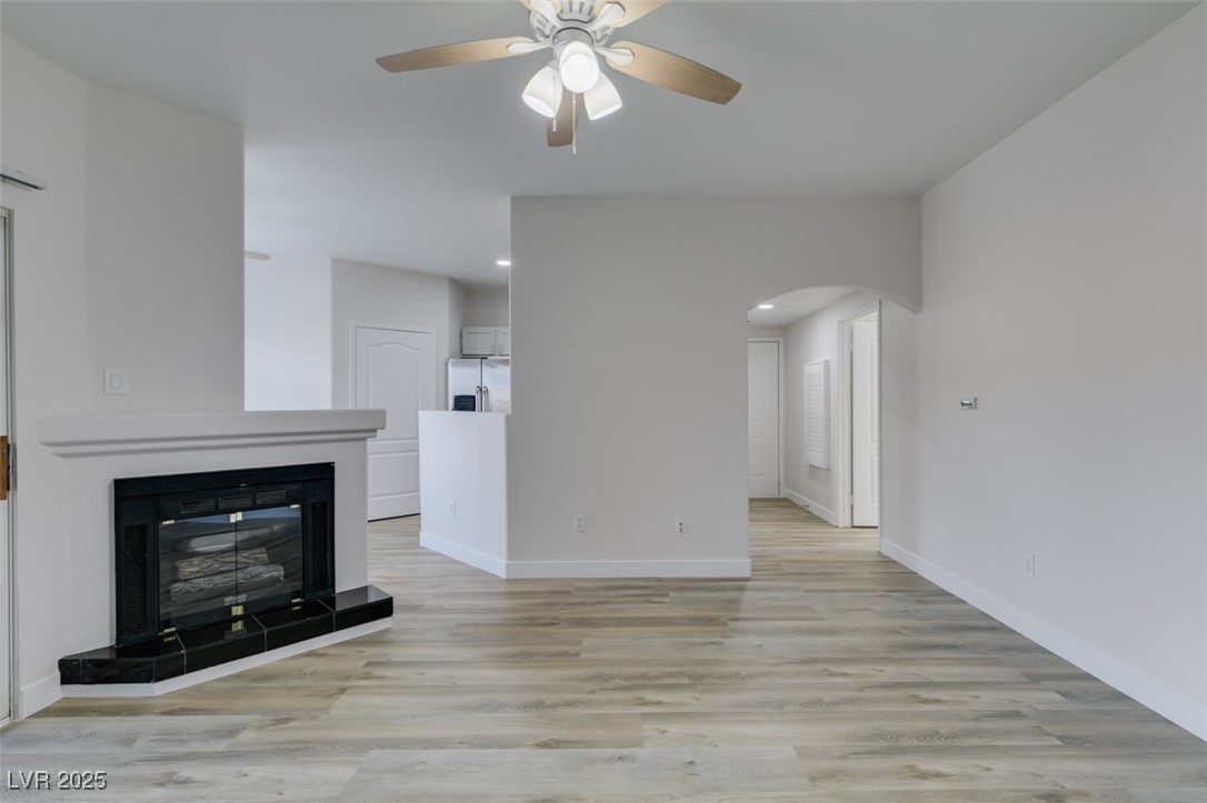 5525 West Flamingo Road, Unit 1028 Las Vegas, NV 89103 - Photo 18 of 42 Unfurnished living room with light wood-type flooring, a tiled fireplace, arched walkways, ceiling fan, and recessed lighting