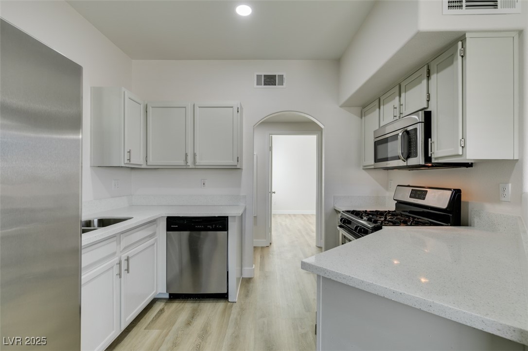 5525 West Flamingo Road, Unit 1028 Las Vegas, NV 89103 - Photo 28 of 42 Kitchen featuring stainless steel appliances, arched walkways, light wood finished floors, light stone countertops, and recessed lighting