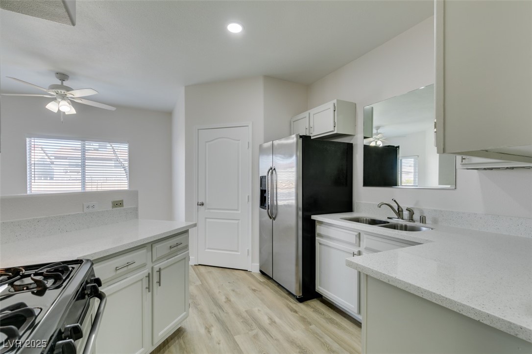 5525 West Flamingo Road, Unit 1028 Las Vegas, NV 89103 - Photo 30 of 42 Kitchen featuring a ceiling fan, gas range oven, light stone countertops, white cabinets, and light wood-style floors