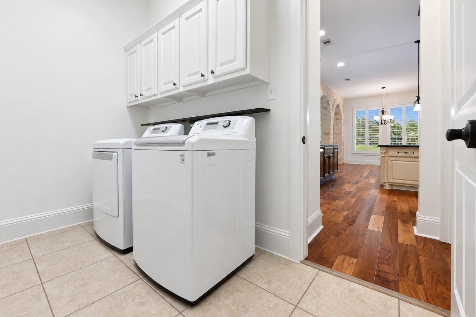 5403 Mesquite Ridge Street Fulshear, TX 77441 - Photo 25 of 42 Conveniently tucked off the kitchen, the laundry room has connections for a full size washer and dryer and white overhead cabinetry with plenty of space for detergents and cleaning supplies. Durable tile flooring makes cleanup simple.