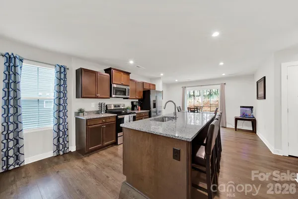 a kitchen with stainless steel appliances granite countertop a stove top oven a sink dishwasher a dining table and chairs with wooden floor