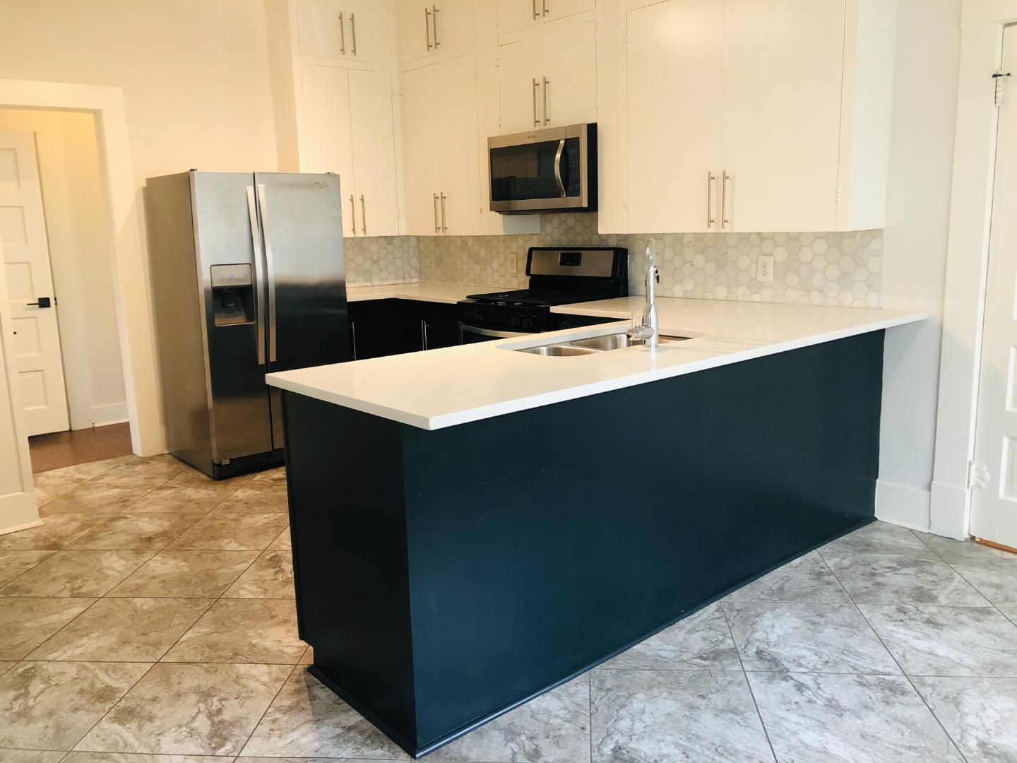 207 West 39th Street, Unit MAIN Austin, TX 78751 - Photo 2 of 7 A contemporary kitchen showcases a spacious island and sleek, contrasting cabinetry with stylish hexagonal tile.