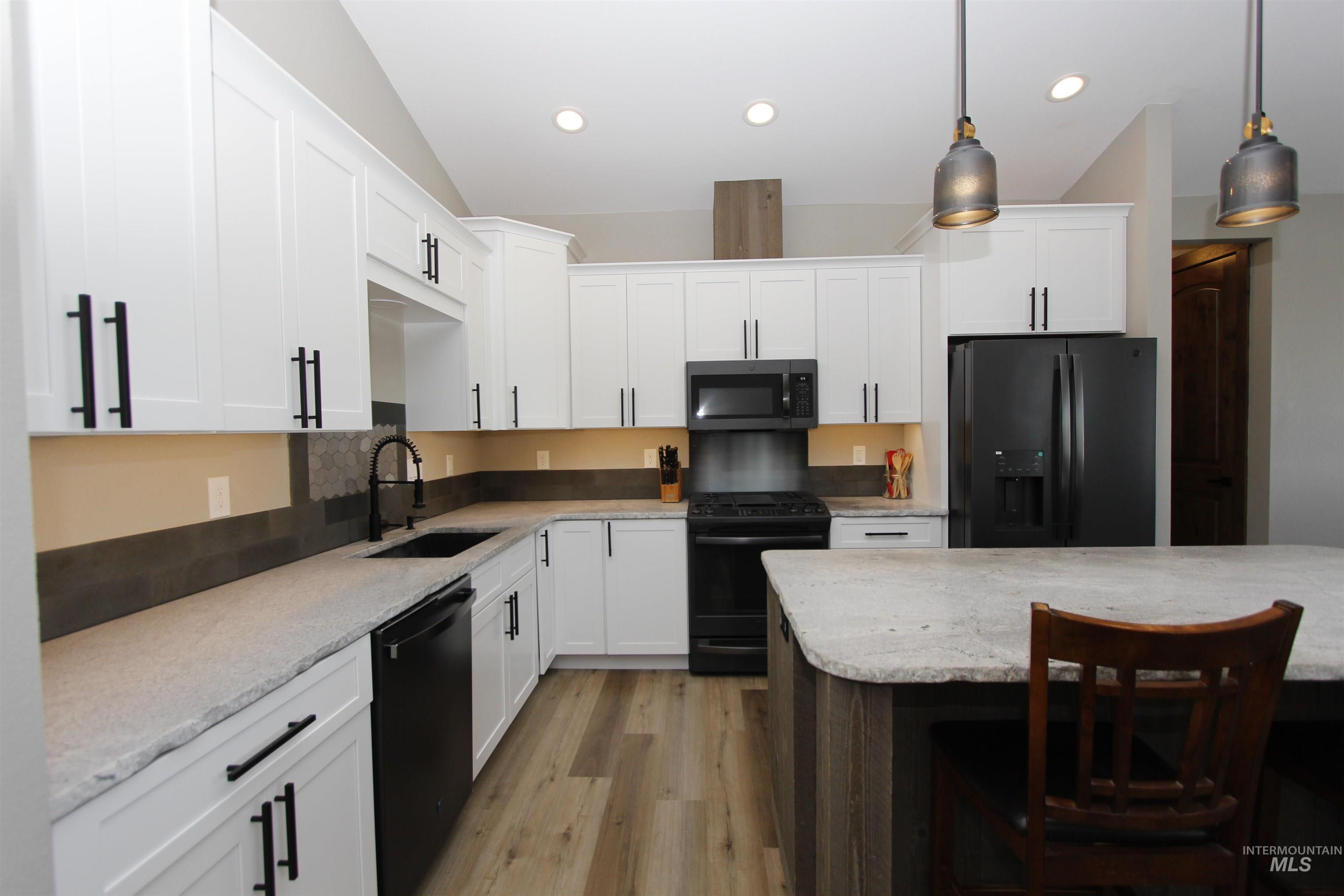 2013 Cedar Avenue Lewiston, ID 83501 - Photo 10 of 46 Kitchen with black appliances, light stone counters, dual tone cabinetry, a breakfast bar, and light wood-type flooring