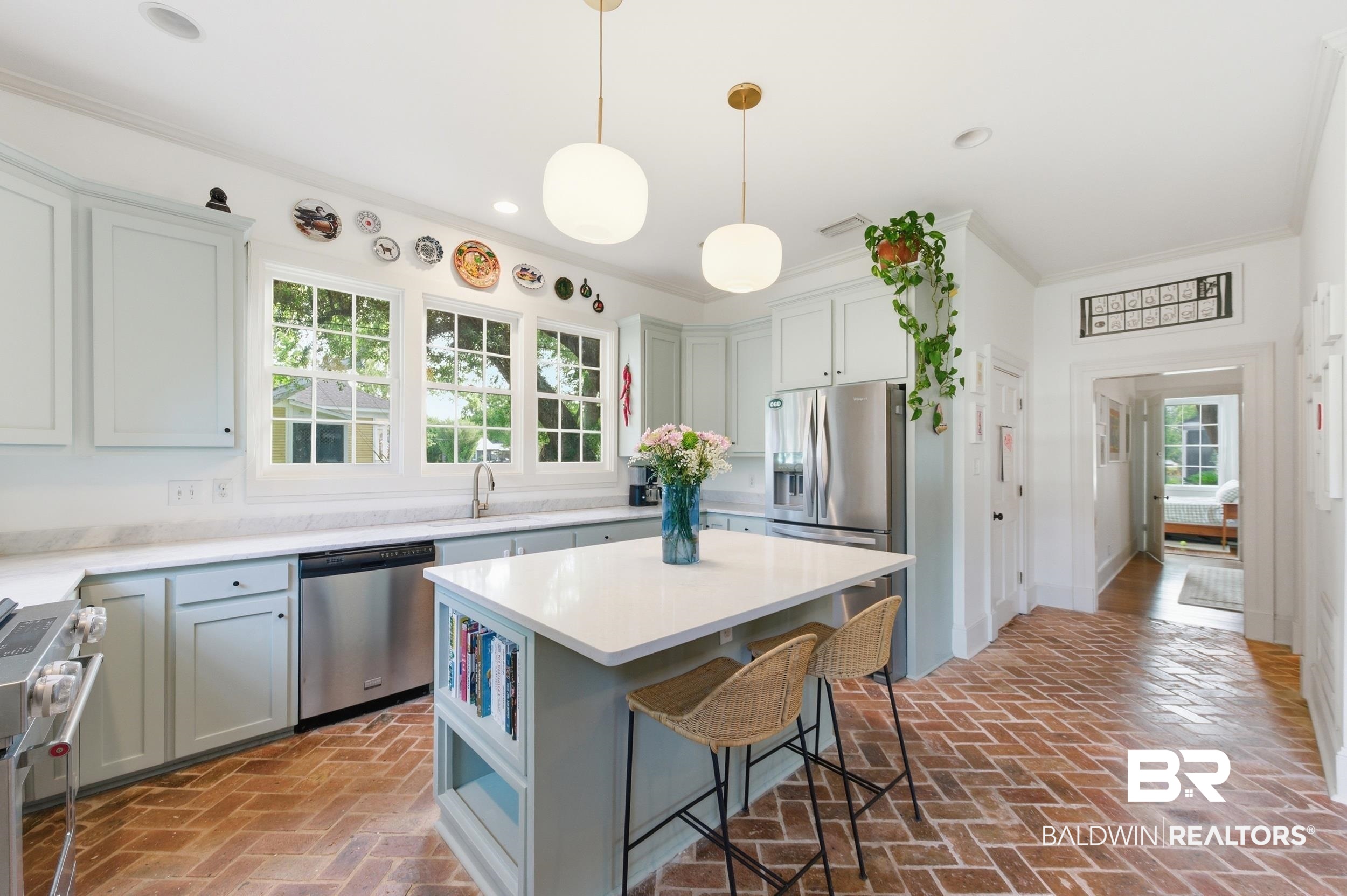350 Charles Street Mobile, AL 36604 - Photo 10 of 52 Kitchen featuring light-toned cabinetry, stainless steel appliances, a center island with seating and integrated shelving, white countertops, and brick-patterned flooring