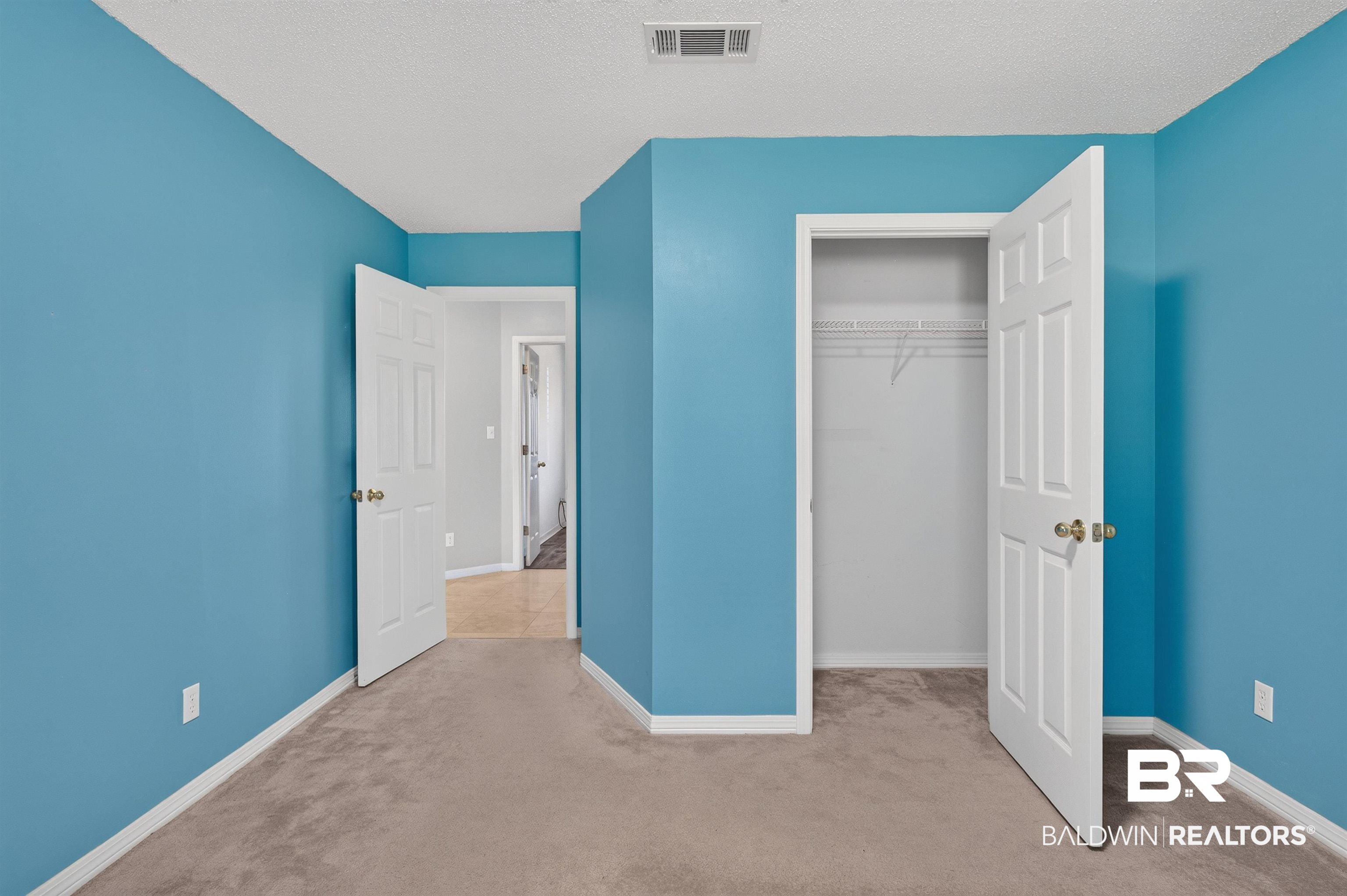 22685 County Road 12 Foley, AL 36535 - Photo 71 of 89 Bedroom featuring a built-in closet with wire shelving, carpet flooring, a white six-panel door, and blue-painted walls with white trim