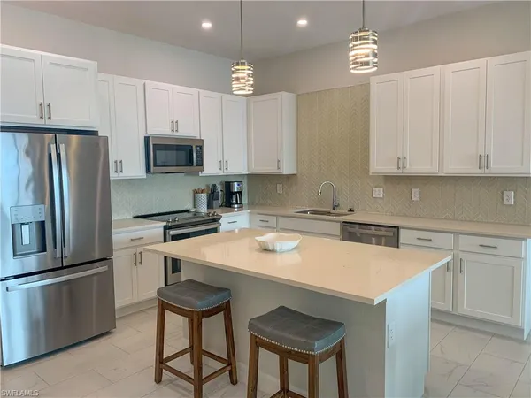 a kitchen with stainless steel appliances a sink a stove a refrigerator cabinets and chairs