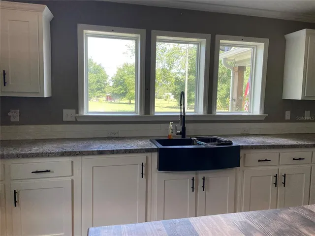 a kitchen with granite countertop a sink white cabinets and a window