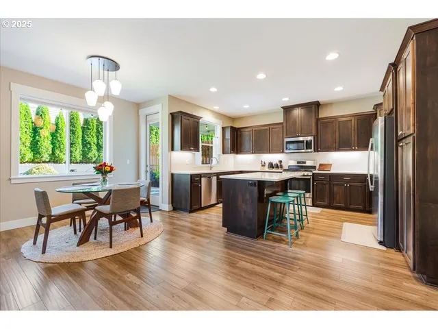 a open kitchen view with stainless steel appliances granite countertop a stove top oven a sink dishwasher a dining table and chairs with wooden floor