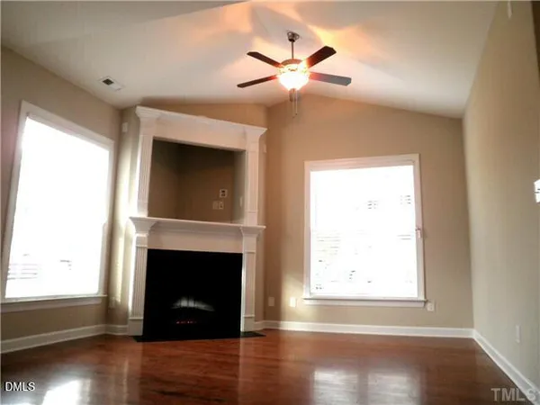 an empty room with wooden floor a fireplace and windows