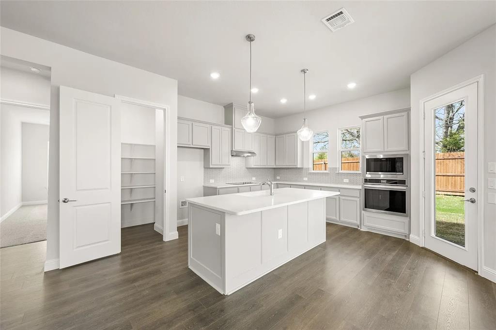 4021 Alpine Street Midlothian, TX 76065 - Photo 6 of 18 Contemporary kitchen featuring a large central island with integrated sink, stainless steel built-in appliances, recessed lighting, and wood-finish flooring