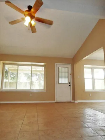 a view of an empty room with chandelier fan and a window