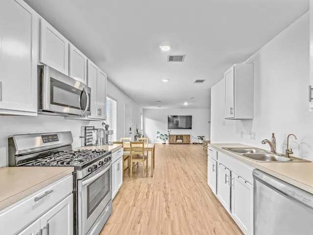 a kitchen with stainless steel appliances granite countertop a stove top oven a sink dishwasher and a refrigerator with wooden floor