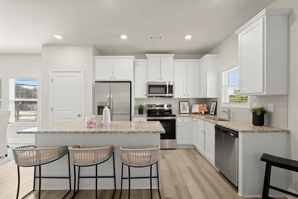 a kitchen with stainless steel appliances granite countertop a stove top oven a sink dishwasher a refrigerator and white cabinets with wooden floor