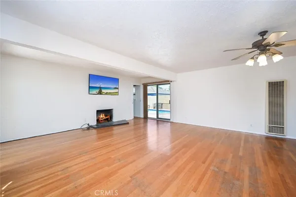 an empty room with wooden floor chandelier fan and windows