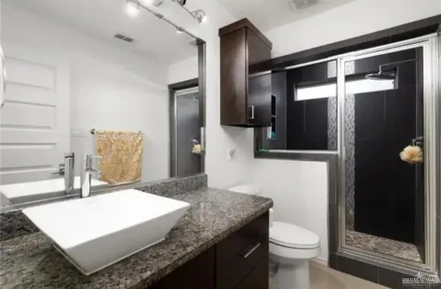a bathroom with a granite countertop sink a toilet and shower