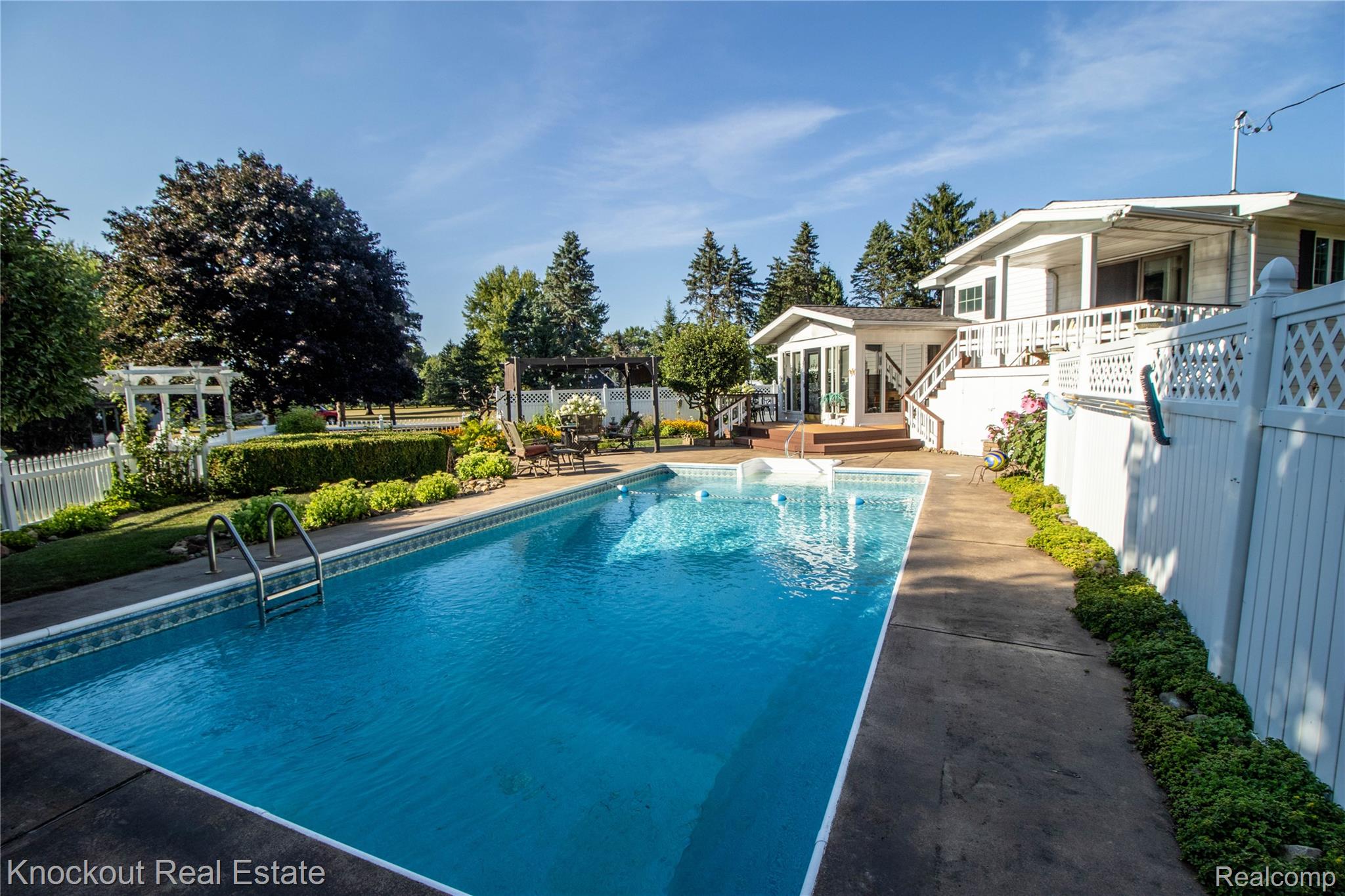 14720 Lincoln Road Chesaning, MI 48616 - Photo 41 of 60 In-ground swimming pool with integrated steps, surrounded by concrete decking and lush landscaping