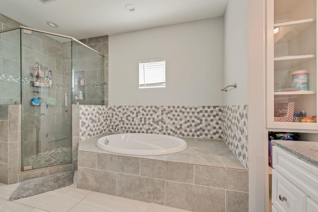 610 Ewing Road Ferris, TX 75125 - Photo 14 of 22 Glass-enclosed shower with tile surround, built-in soaking tub with mosaic tile accents, and built-in white cabinetry with glass display doors
