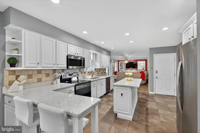 a kitchen with stainless steel appliances kitchen island granite countertop a refrigerator oven a sink dishwasher and white cabinets with wooden floor