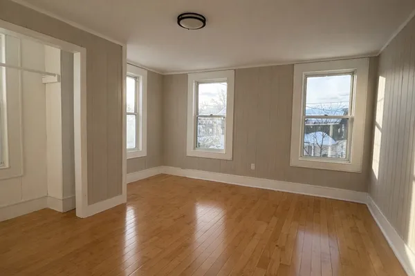 a view of an empty room with wooden floor and a window