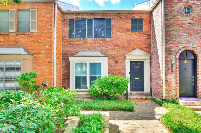 a view of a brick house with a yard plants and large tree